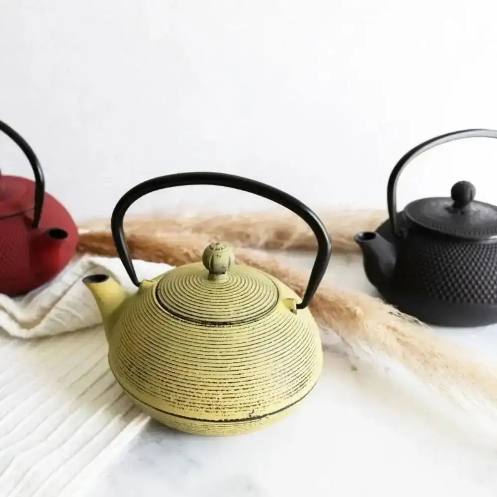 Three cast iron teapots in different colors on a light surface.