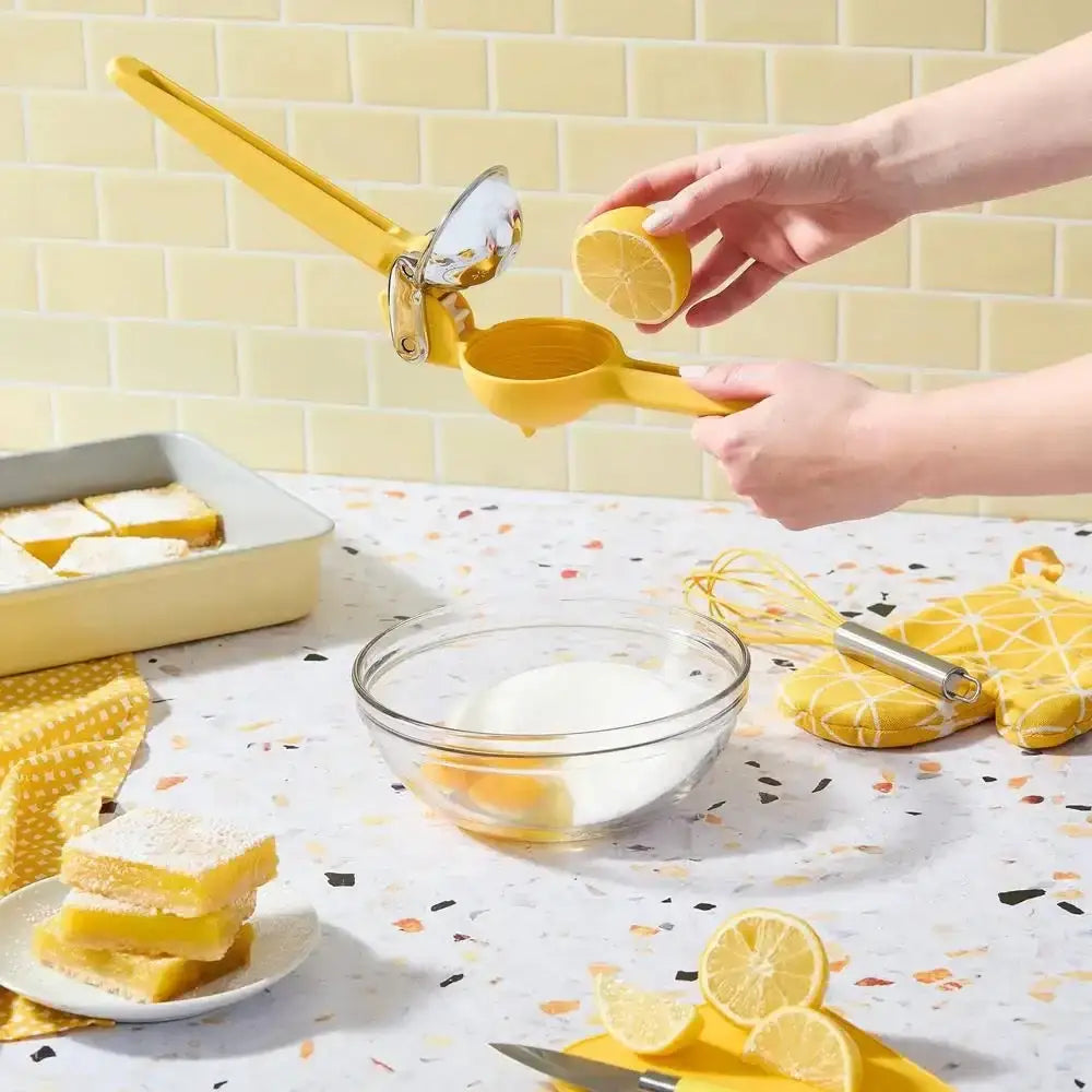 Person using a yellow lemon squeezer with lemons and baking ingredients on a kitchen counter.