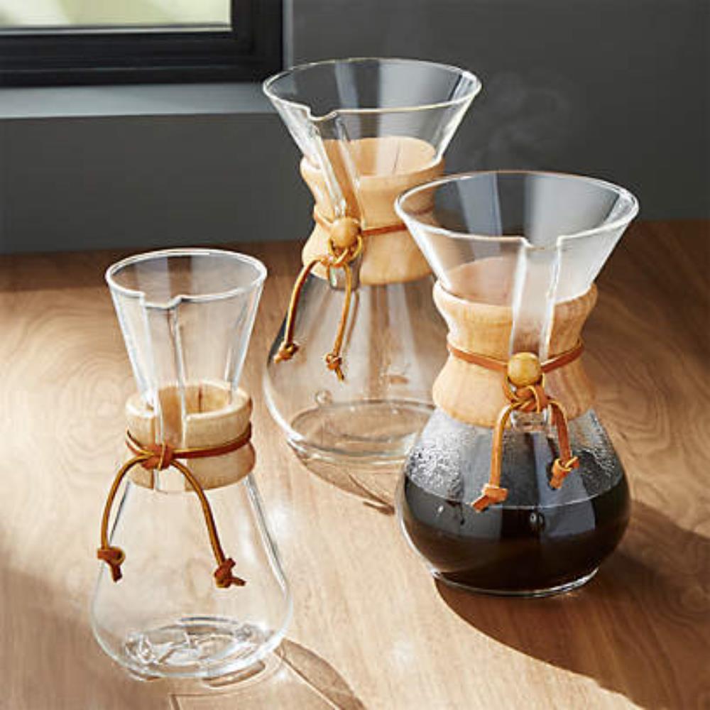 Three glass coffee makers with wooden collars on a wooden surface.