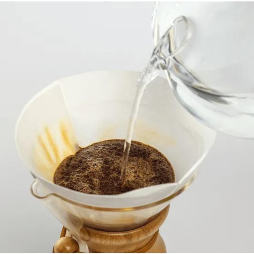Pouring water into a coffee filter with ground coffee on a white background