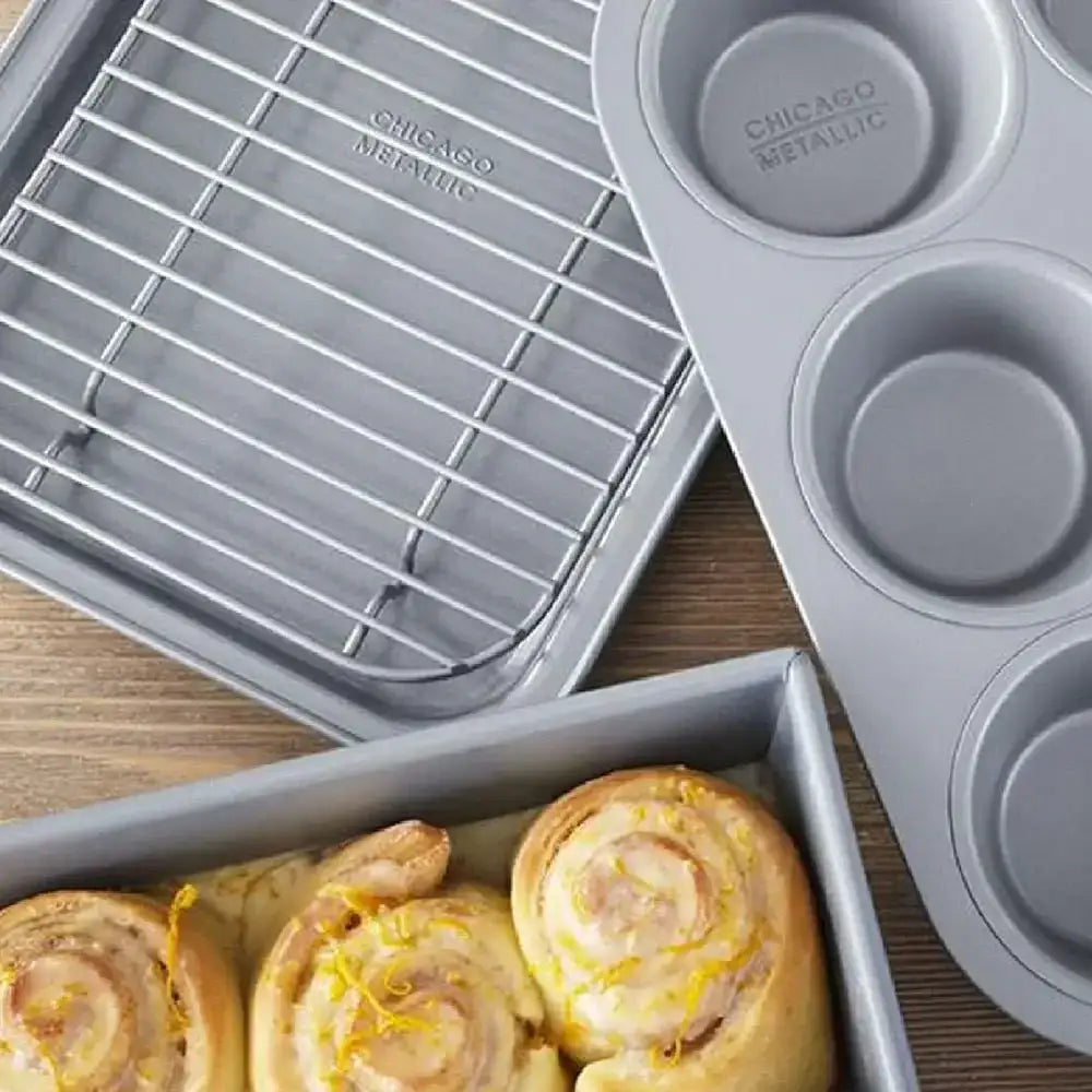 Chicago Metallic non-stick bakeware set with muffin pan, cooling rack, and rolls on wood table