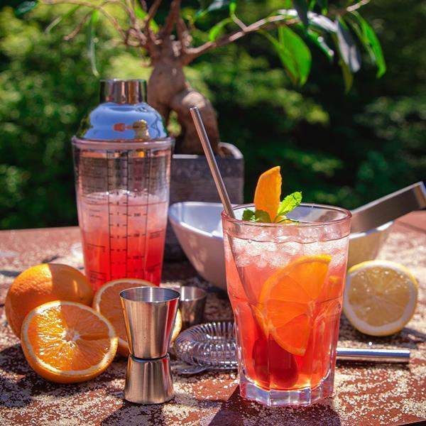Cosmopolitan cocktail barware set with shaker, jigger, citrus, and fresh cocktail outdoors
