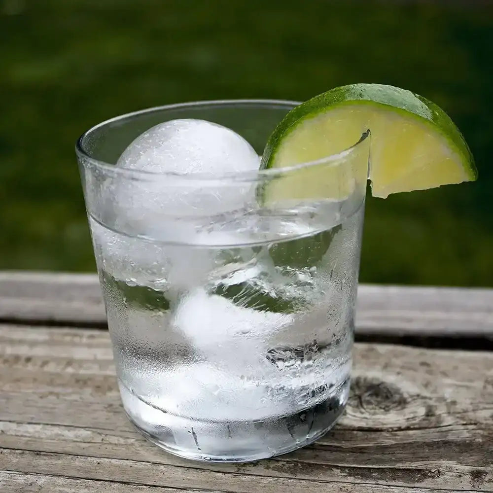 Glass of water with a round ice ball and lime wedge on wood table, kitchenware from Cookin Stores