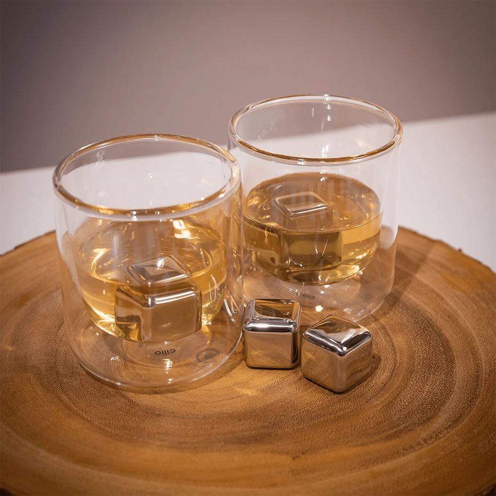 Two glasses with liquid and metal cubes on a wooden surface