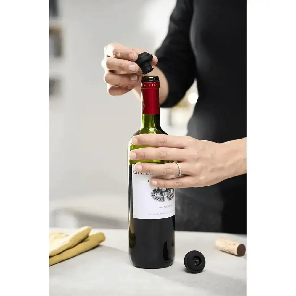 Person opening a bottle of red wine with a corkscrew on a light surface.