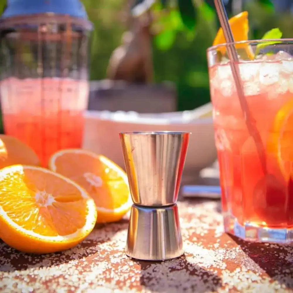 Cocktail with oranges and a jigger on a sandy surface with blurred outdoor background