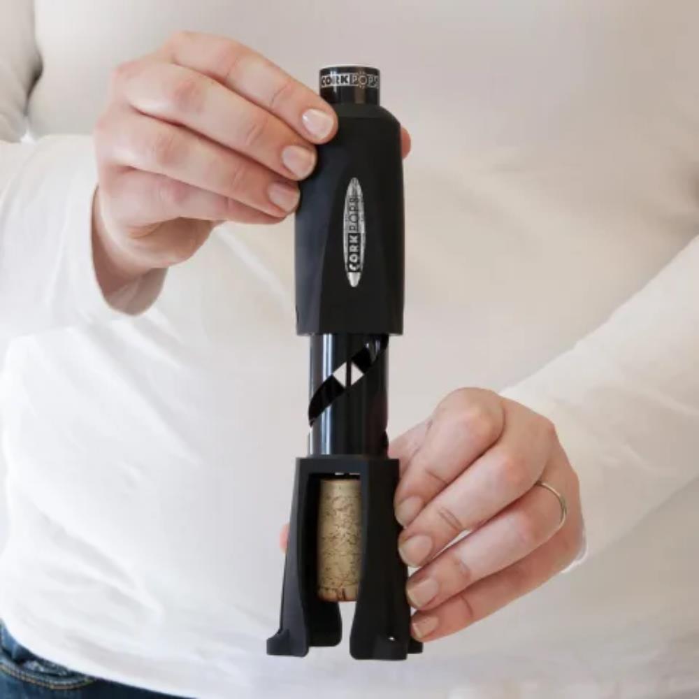 Person using a black corkscrew to remove a cork from a bottle against a white background