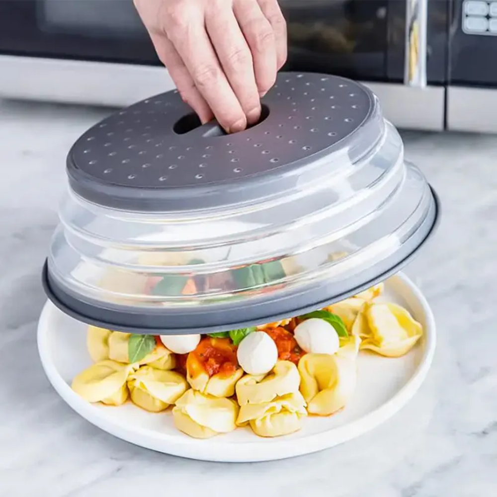 Collapsible food cover being placed over a plate of pasta with a hand holding the top.