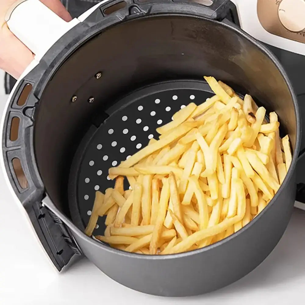 Black perforated air fryer basket with golden french fries on a creative cooking round silicone air fryer mat 20cm