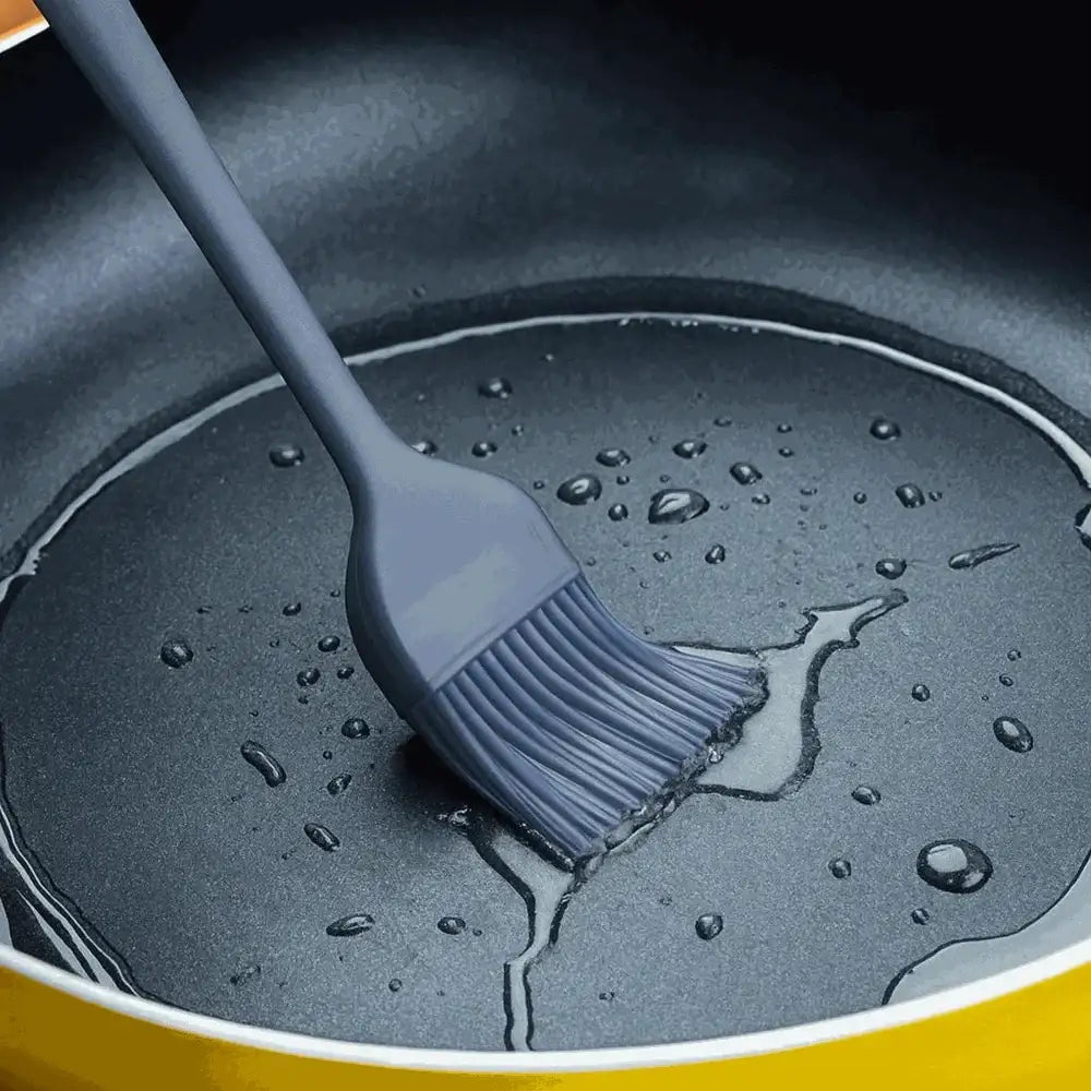 Gray silicone brush in a frying pan with oil and water droplets