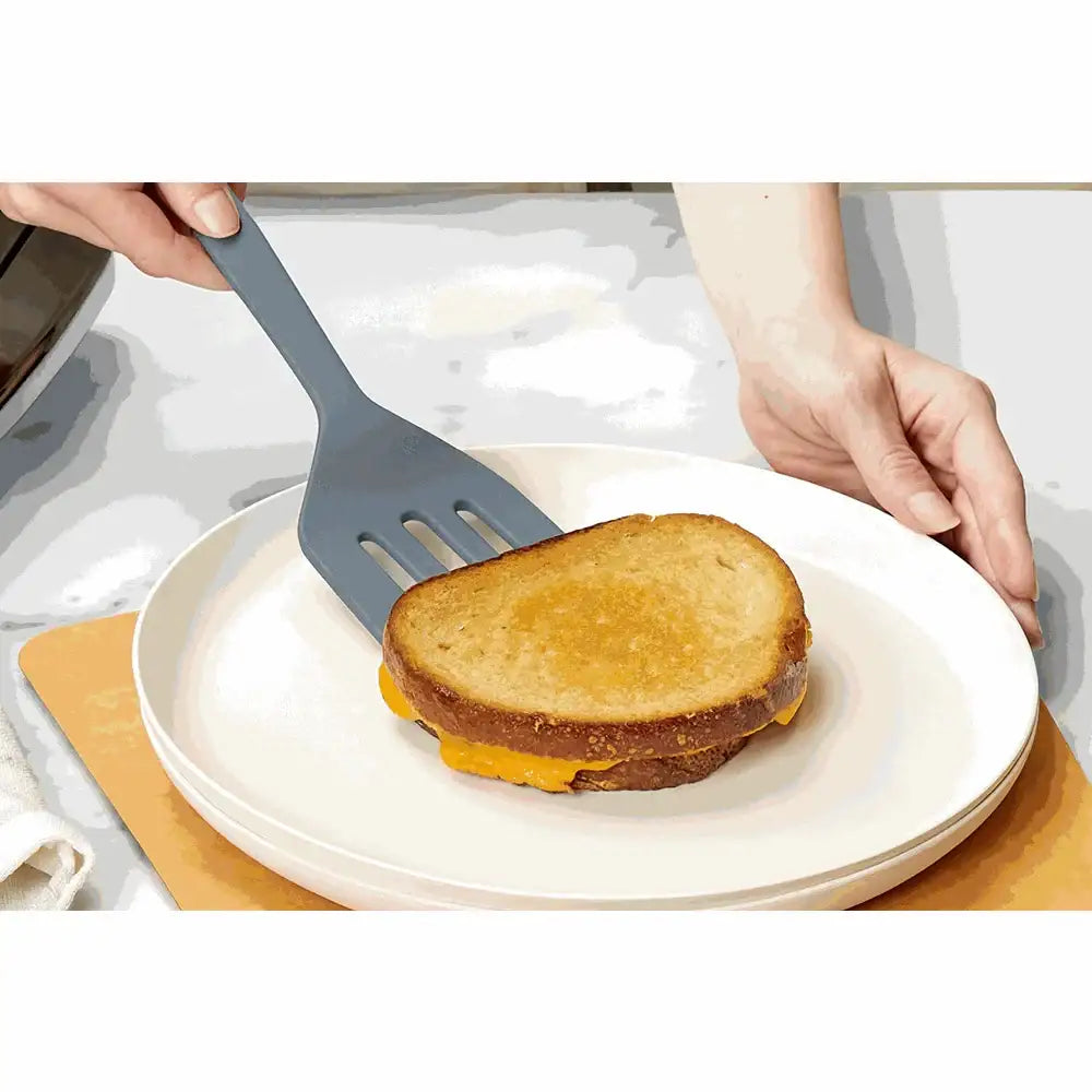 Hand using a spatula to lift a sandwich on a white plate