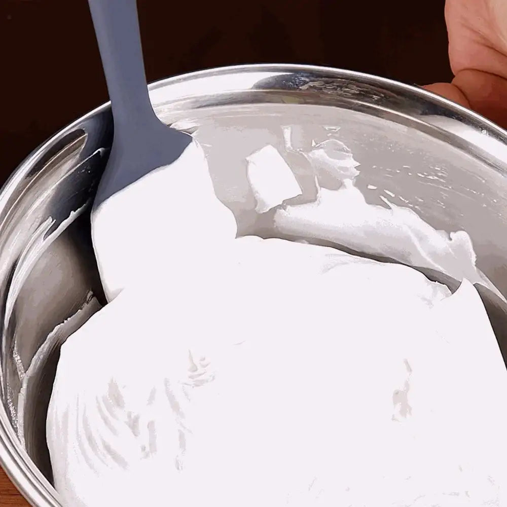 White frosting being stirred in a metal bowl with a spatula.