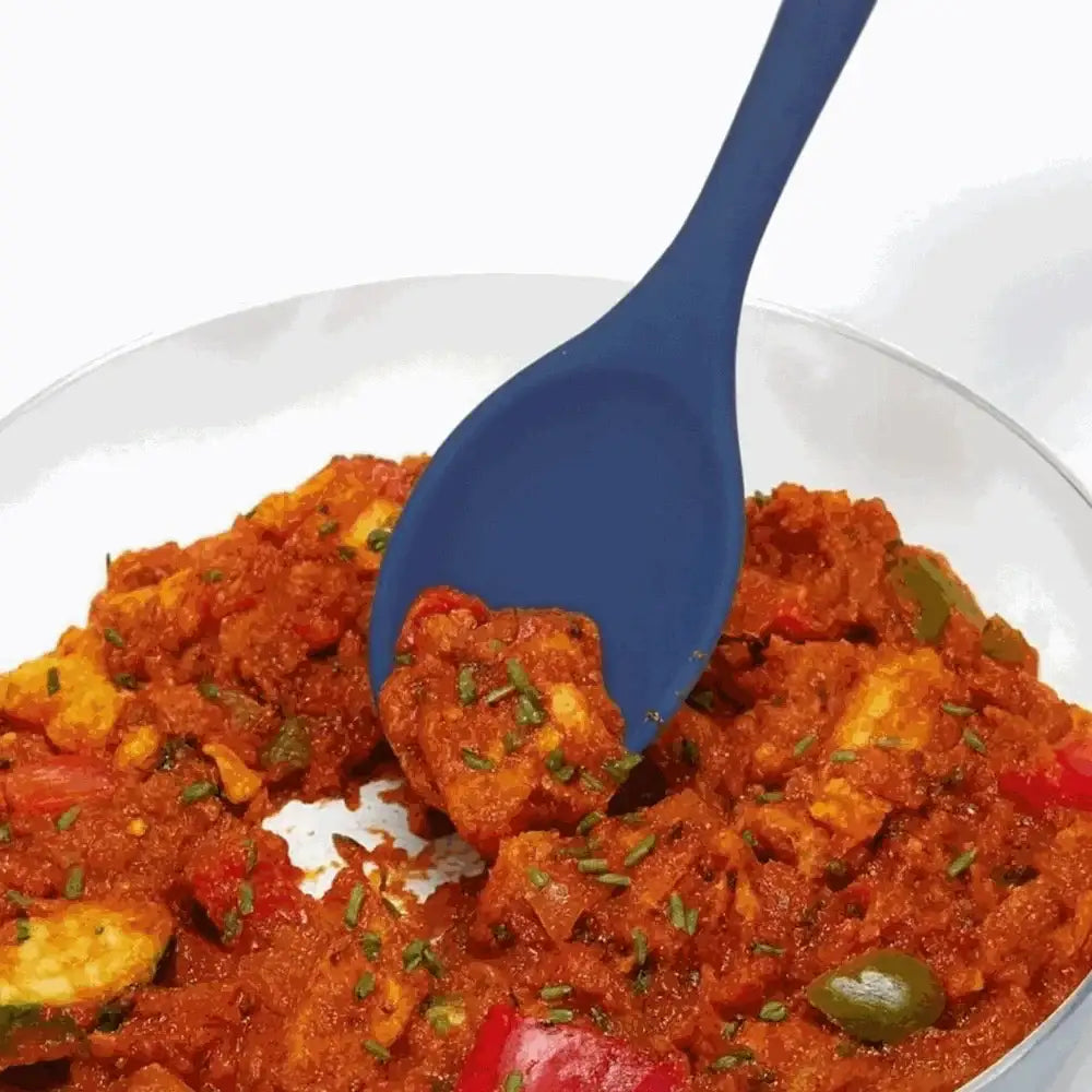Grey silicone cooking spoon scooping vegetable stew from a clear bowl on white background