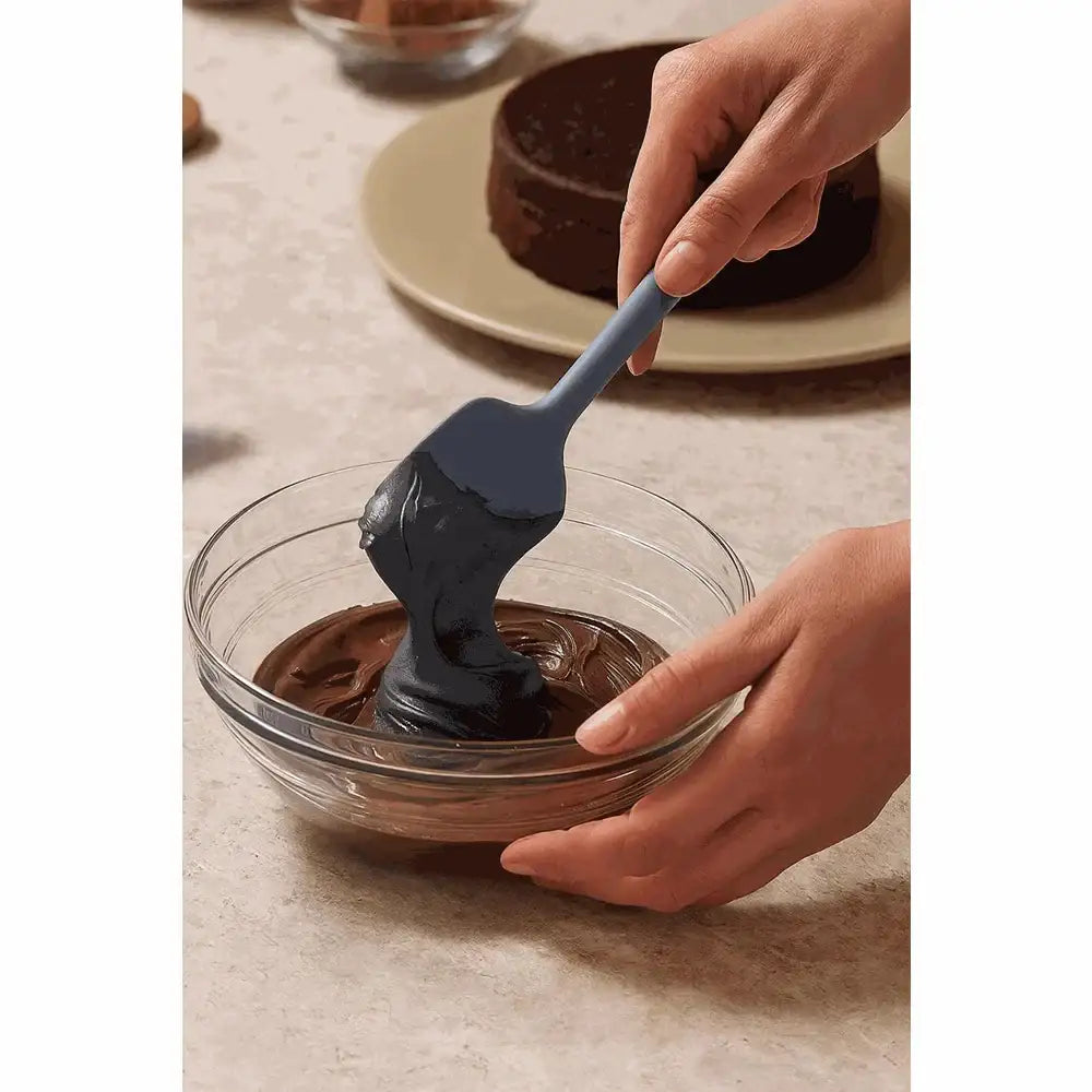 Grey silicone square spoon mixing chocolate batter in a glass bowl on a kitchen counter