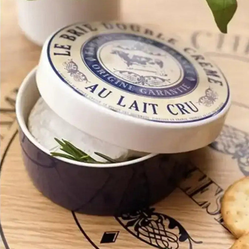 Jar of Le Brie Double Crème Au Lait Cru on a wooden board with crackers and a plant.