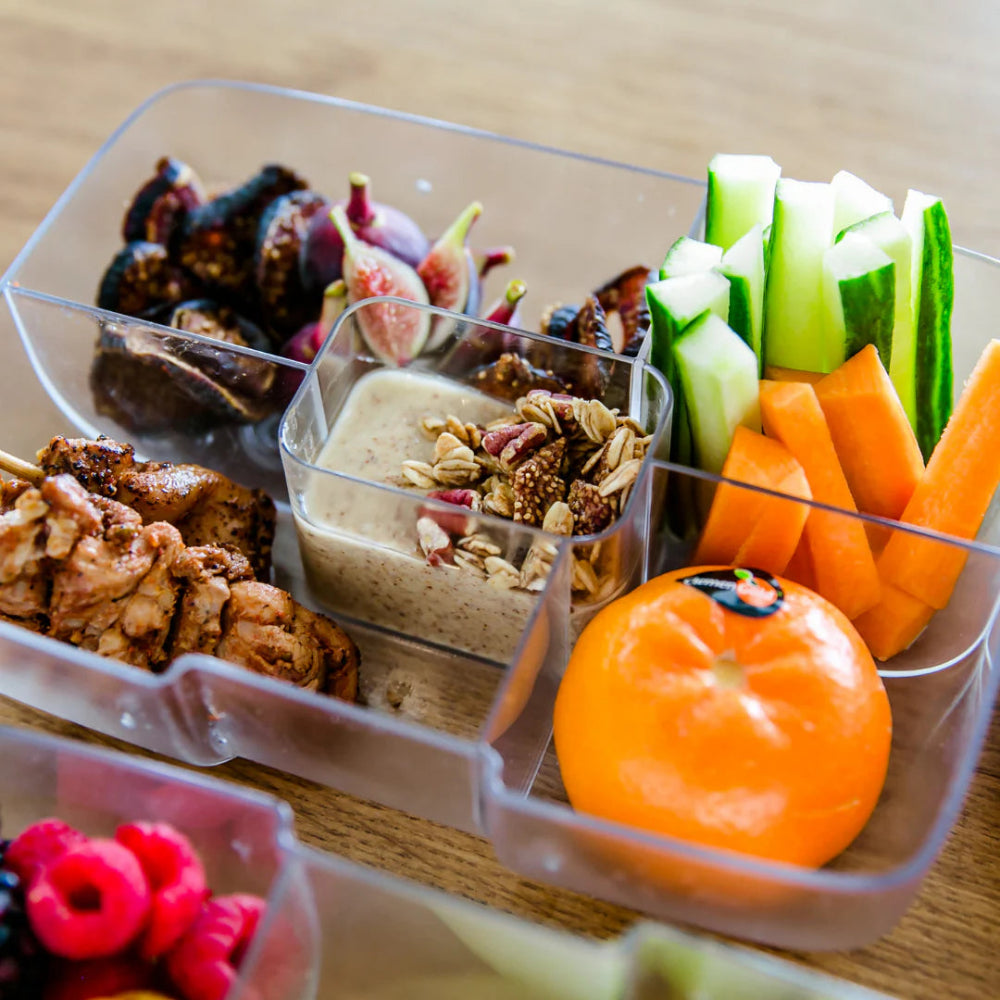 Lunchbox insert with various different foods on a wooden surface 