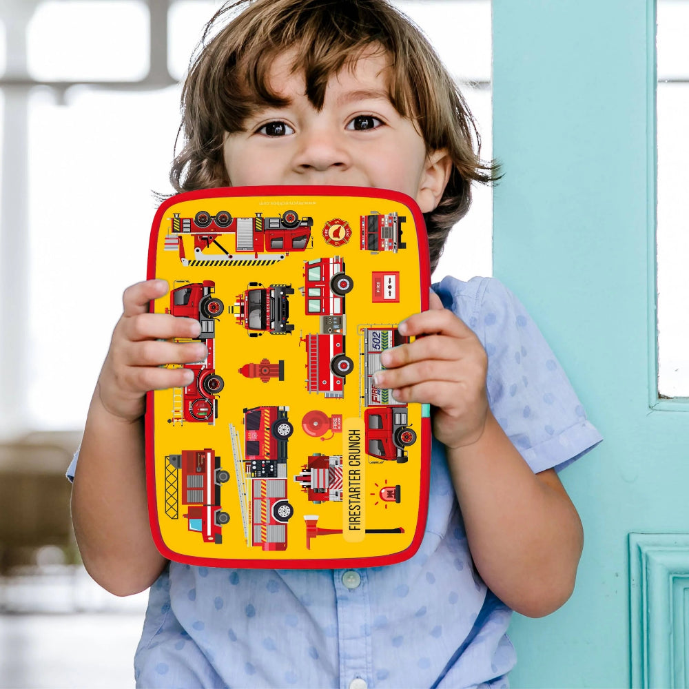 Child holding a yellow lunchbox with a firetruck design on a blurred background