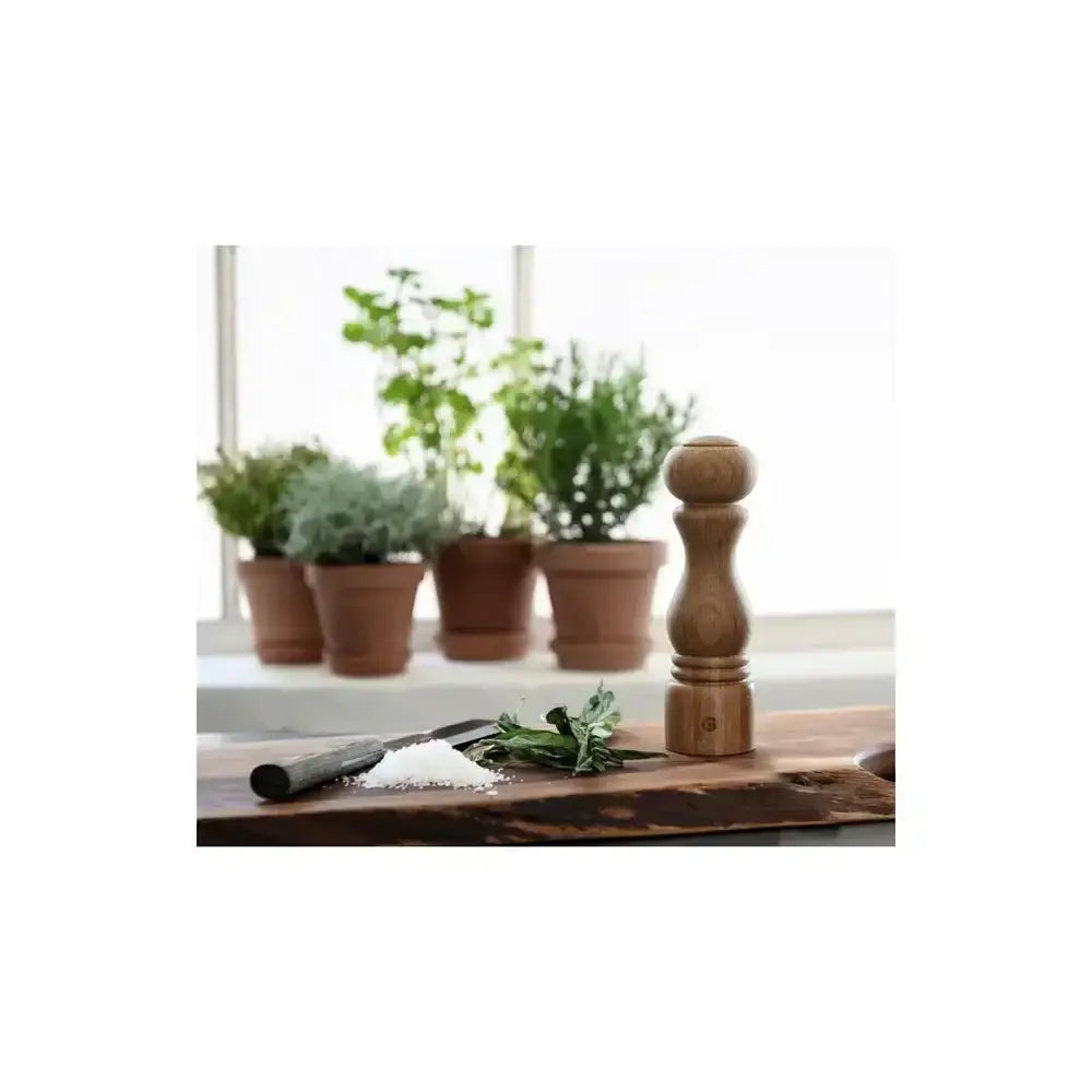 Wooden pepper grinder on a wooden surface with plants in the background