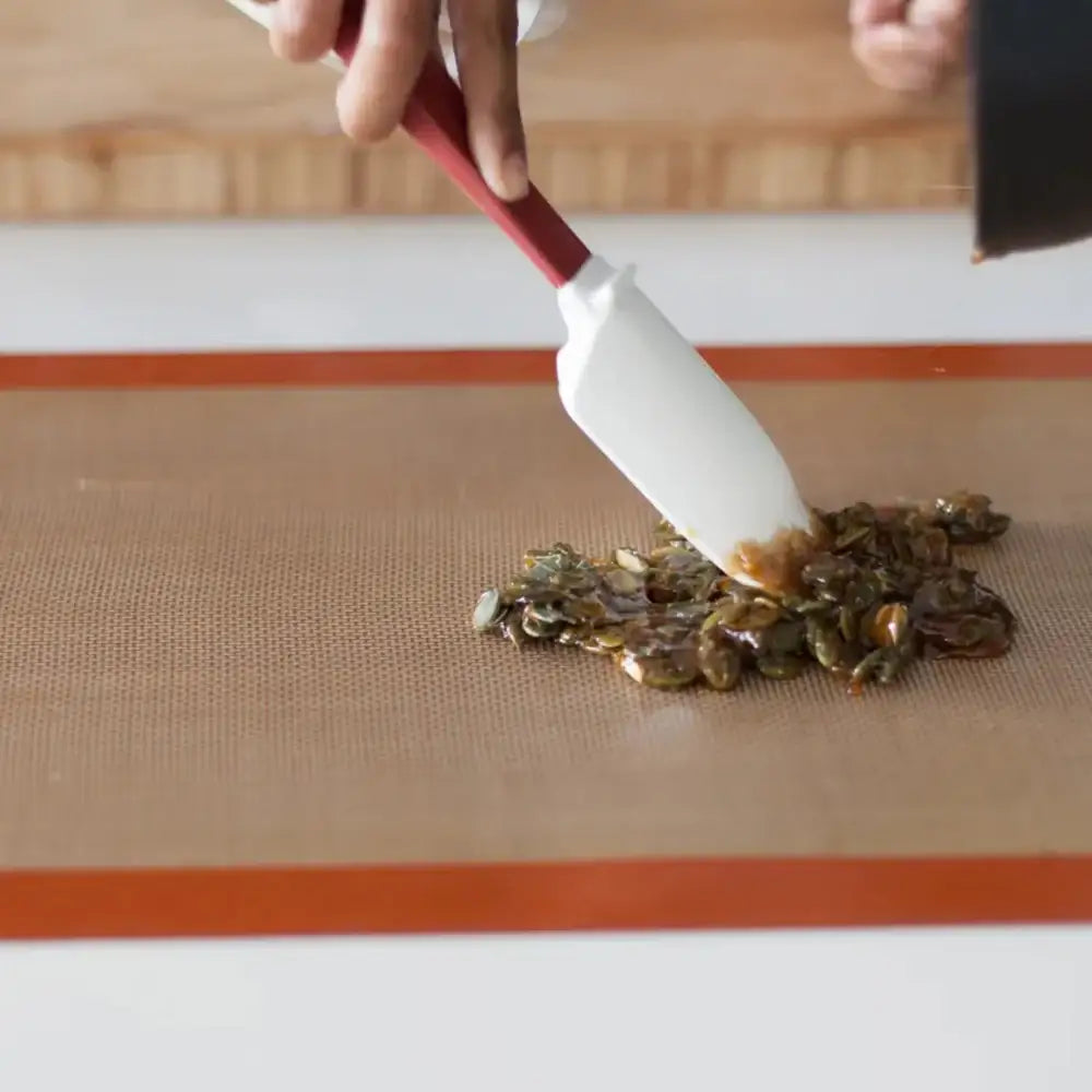Person using a spatula to spread a mixture on a silicone mat.