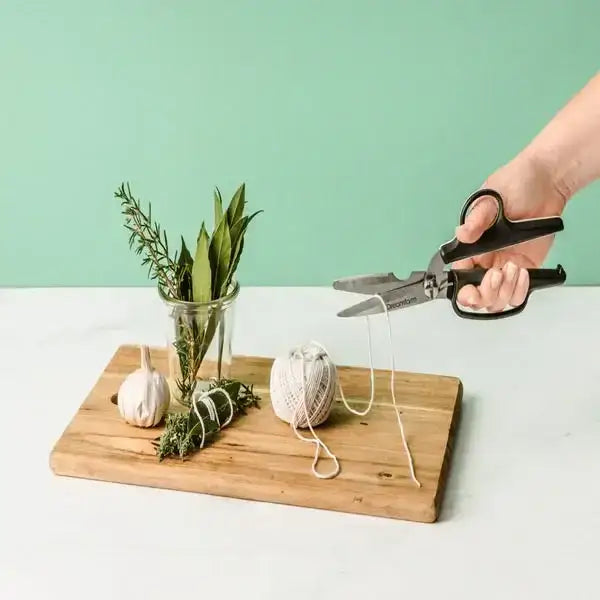 Dreamfarm Bishears kitchen scissors cutting twine on a wooden board with herbs at Cookin Stores