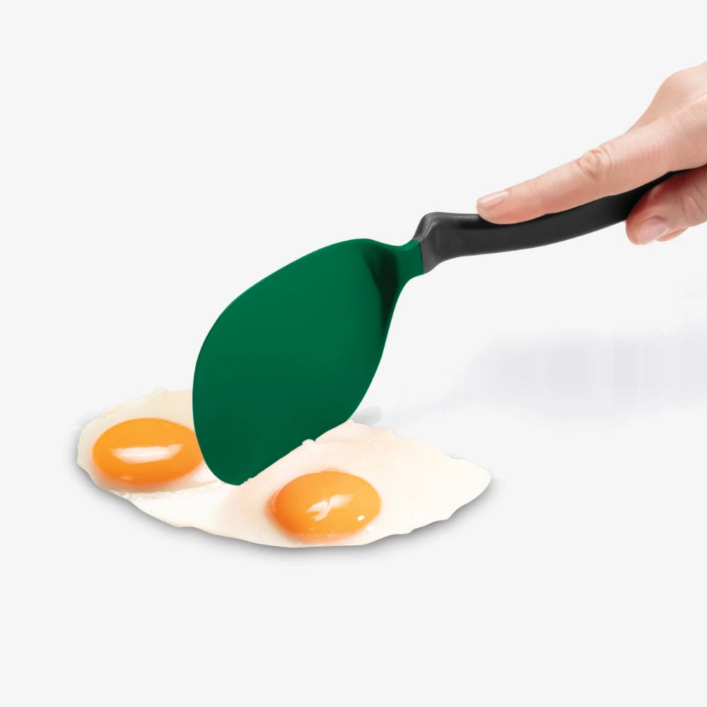 A hand holding a green silicone spatula with a black handle, lifting a fried egg from a white plate against a light gray background.