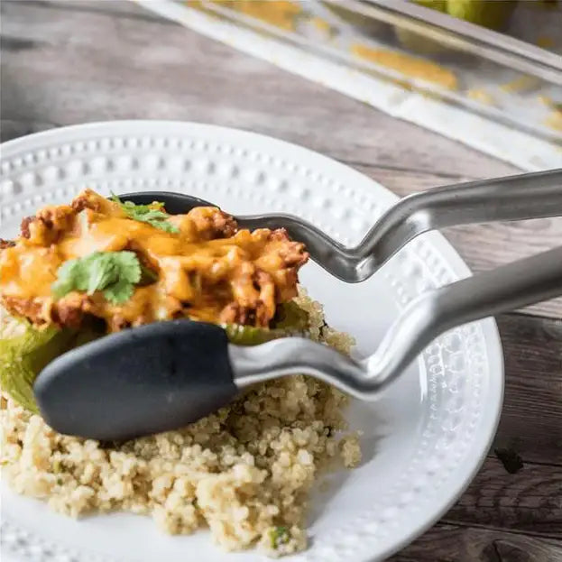 tongs lifting a serving of creamy pasta from a white plate on a wooden table.