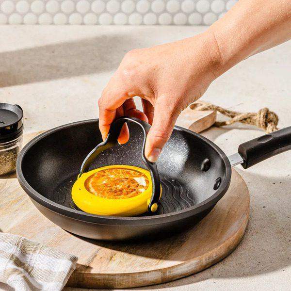 Hand using Dreamfarm Flegg egg flipper to lift cooked egg in nonstick frying pan, Cookin Stores kitchenware.