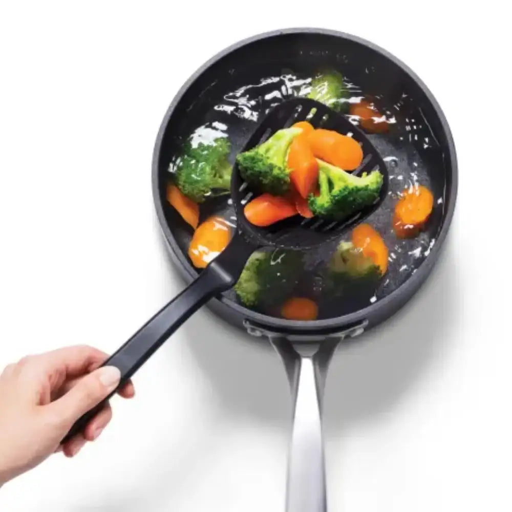 Person using a spatula to serve vegetables from a frying pan on a white background