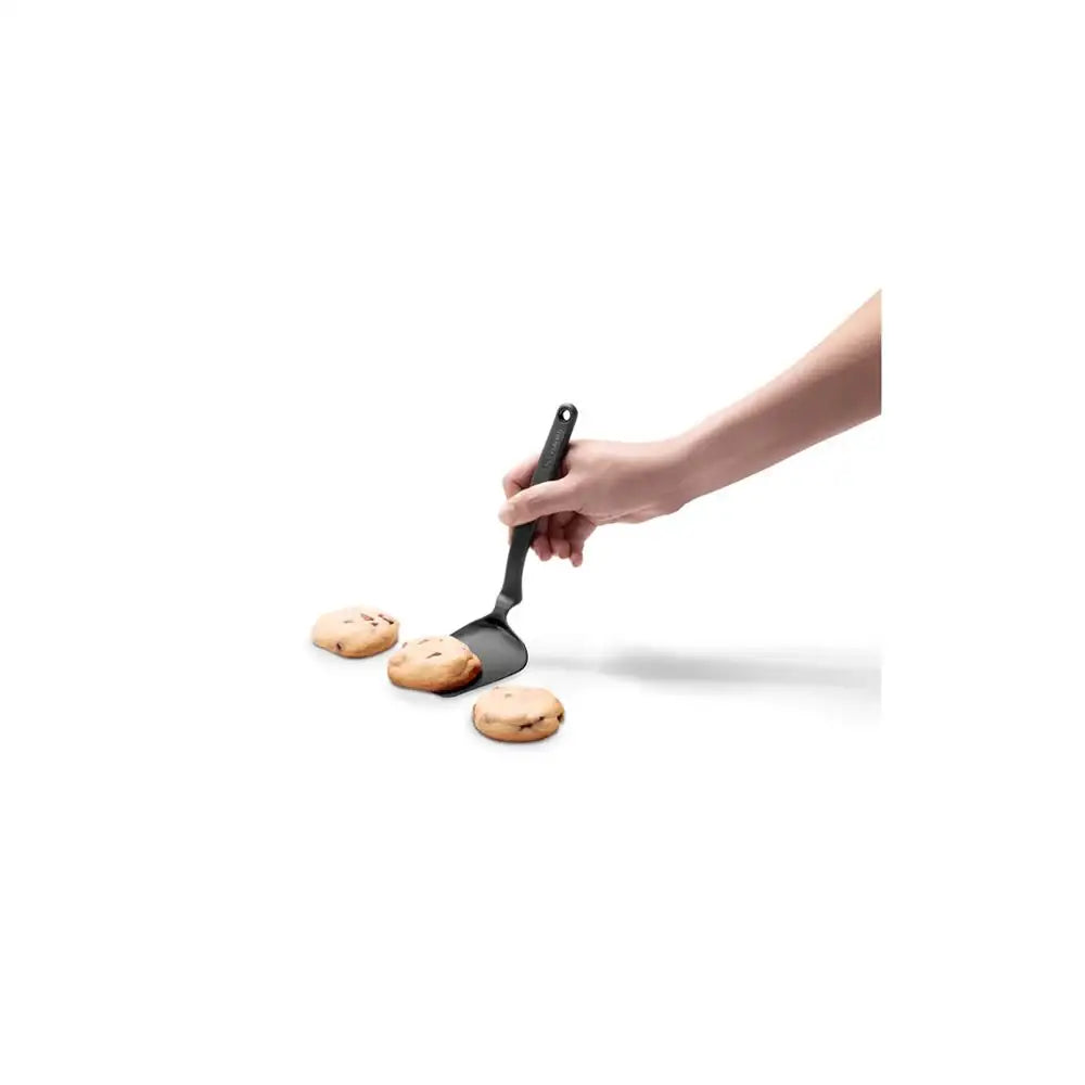 Hand using a black spatula to flip cookies on a white background