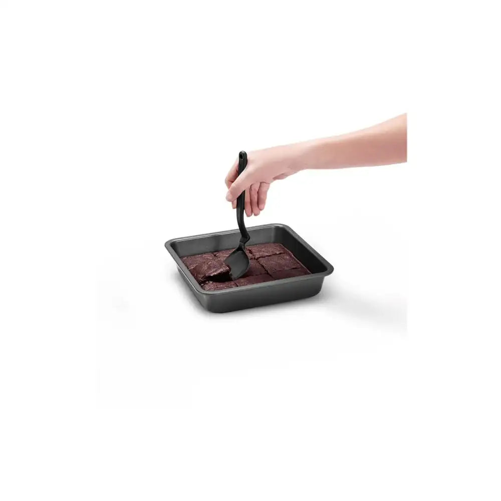 Hand using a spatula to serve brownies from a baking tray on a white background