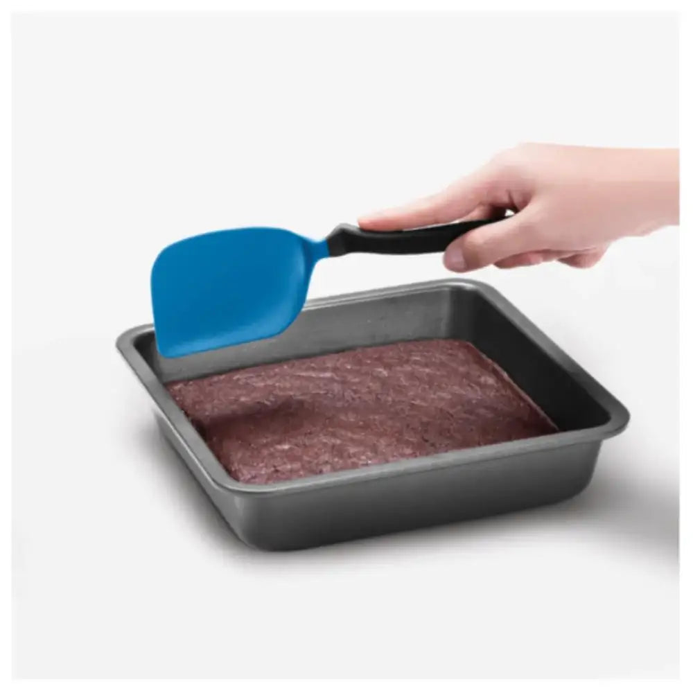 Hand using a blue spatula to lift brownies from a baking pan on a white background