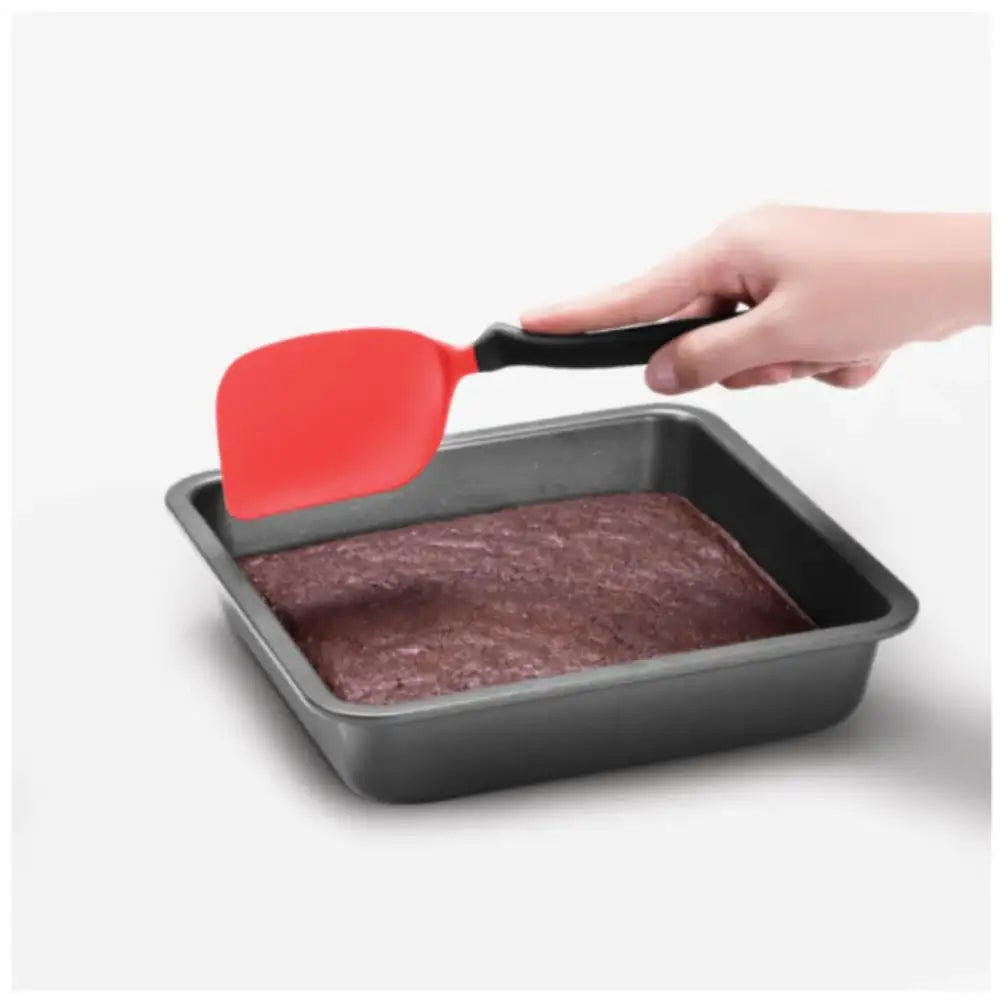 Hand using a red spatula to lift brownies from a baking pan on a white background