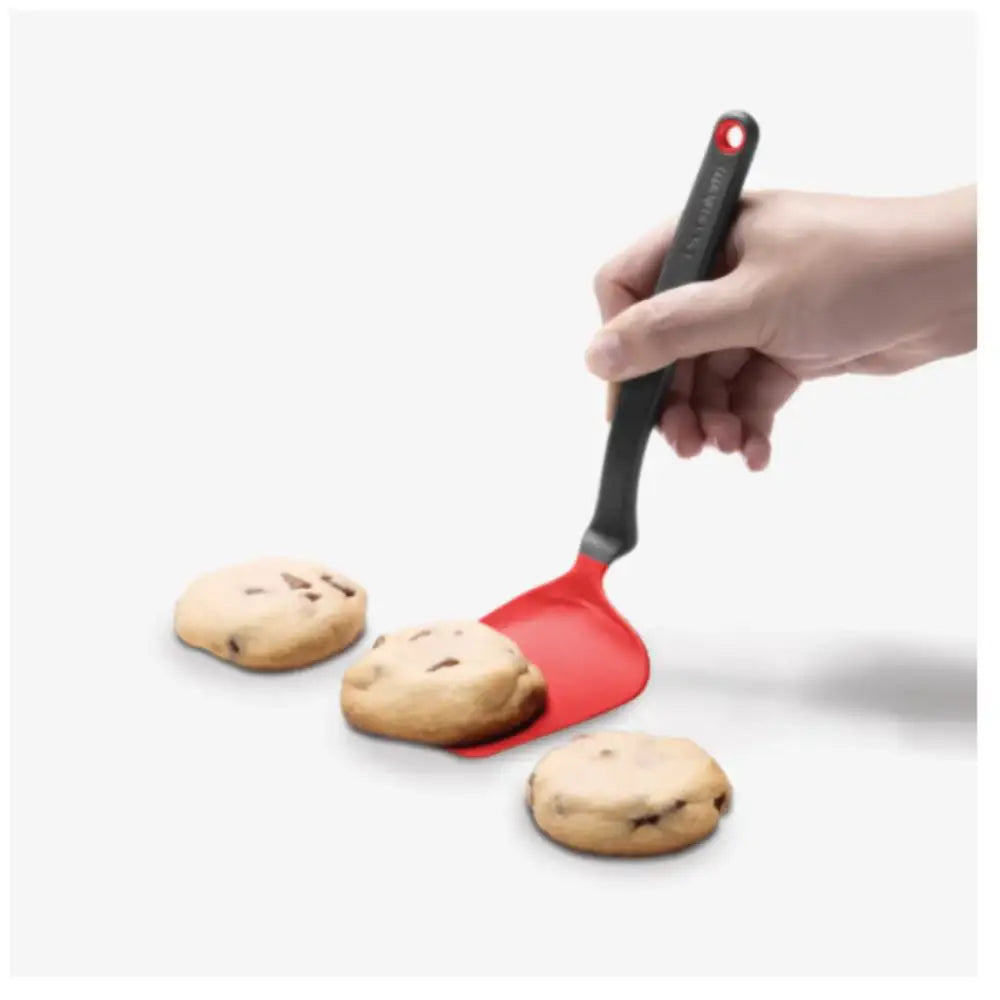 Hand using a red spatula to lift cookies from a baking tray on a white background
