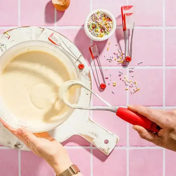 Person mixing batter with Dreamfarm Mini Flisk Whisk in red on pink tile kitchen surface