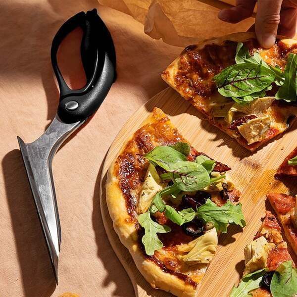 Black pizza scissors beside sliced vegetable pizza on wooden board
