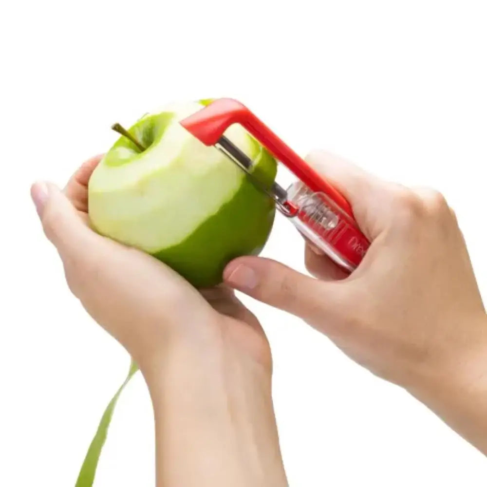 Person using a red apple peeler to remove skin from a green apple on a white background