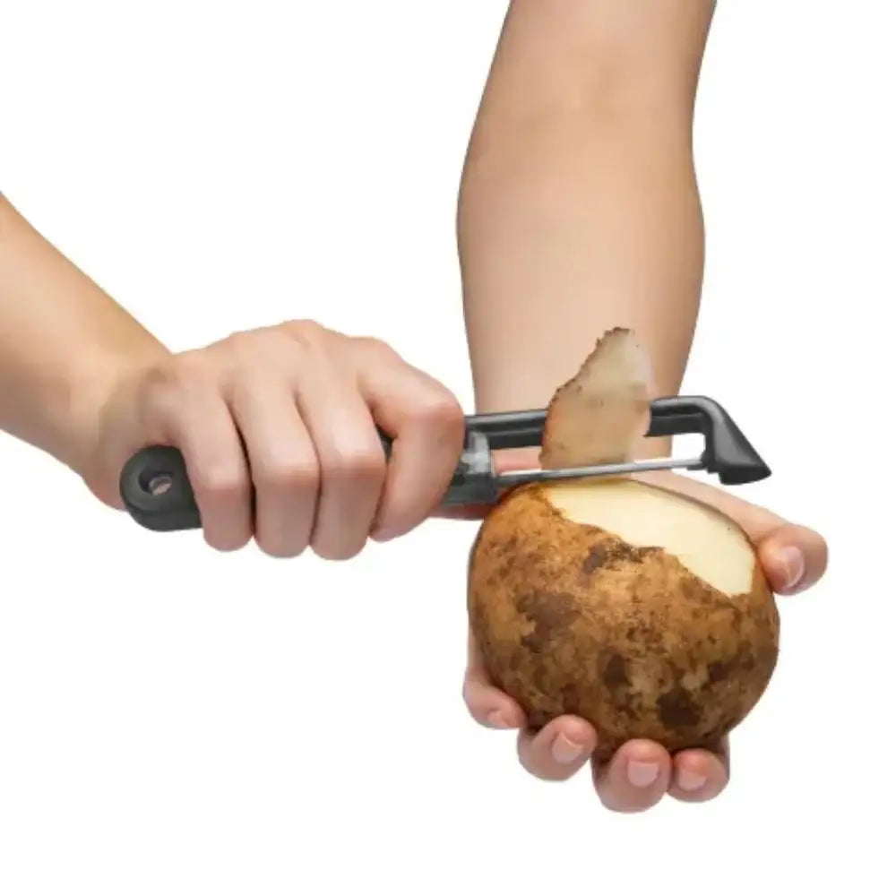 Person peeling a potato with a peeler on a white background