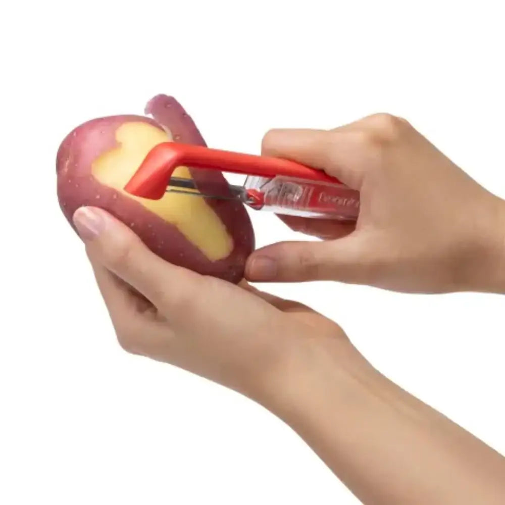 Person peeling a red potato with a red peeler on a white background