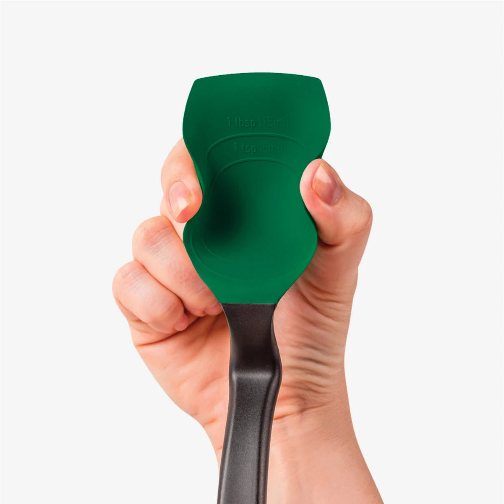 A hand holding a green silicone spatula with a black handle against a light gray background.
