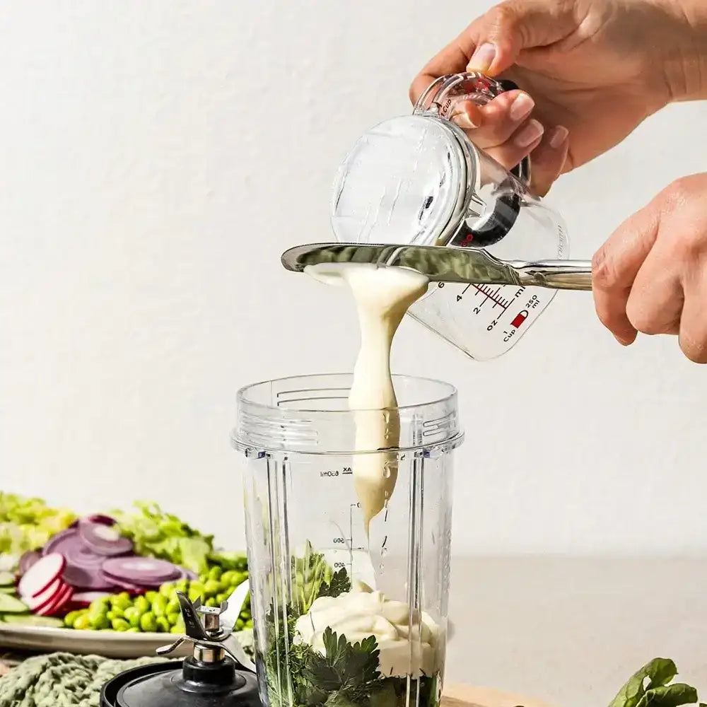 Person pouring a liquid into a blender with ingredients on a table