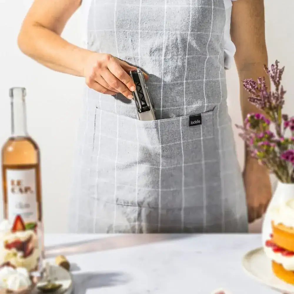 Person in checkered apron holding Dreamfarm mechanical wine opener in kitchen setting, Cookin Stores kitchenware.
