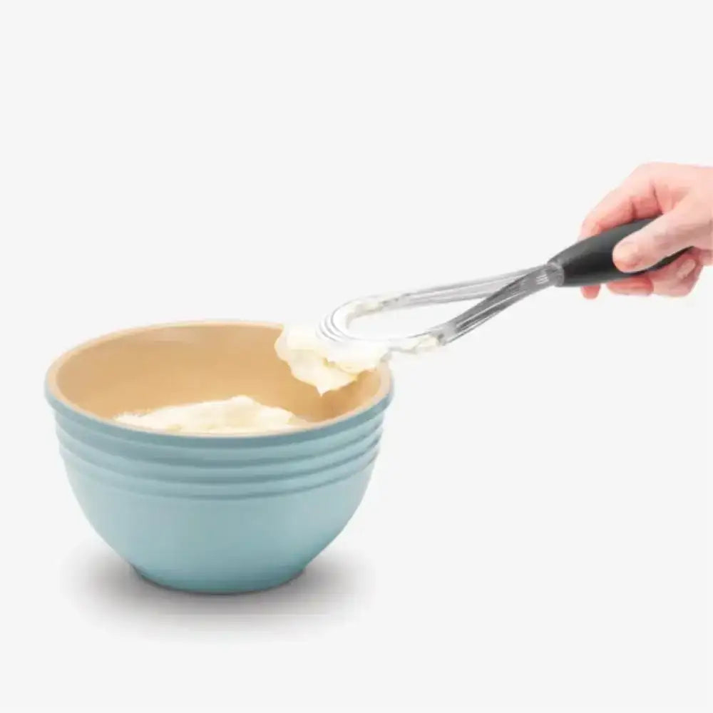 Person using a spatula to transfer cream from a blue bowl onto a beige surface.