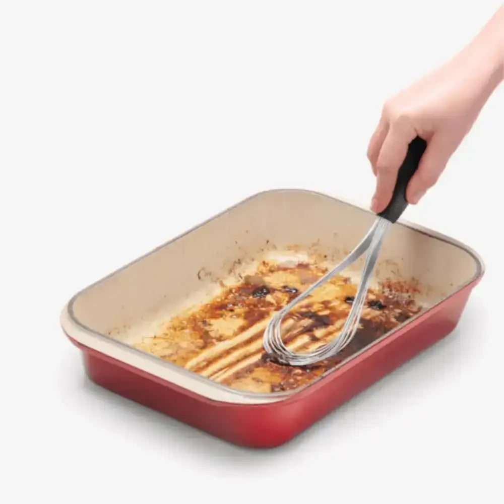 Red rectangular baking dish with a hand using a spoon to serve food.