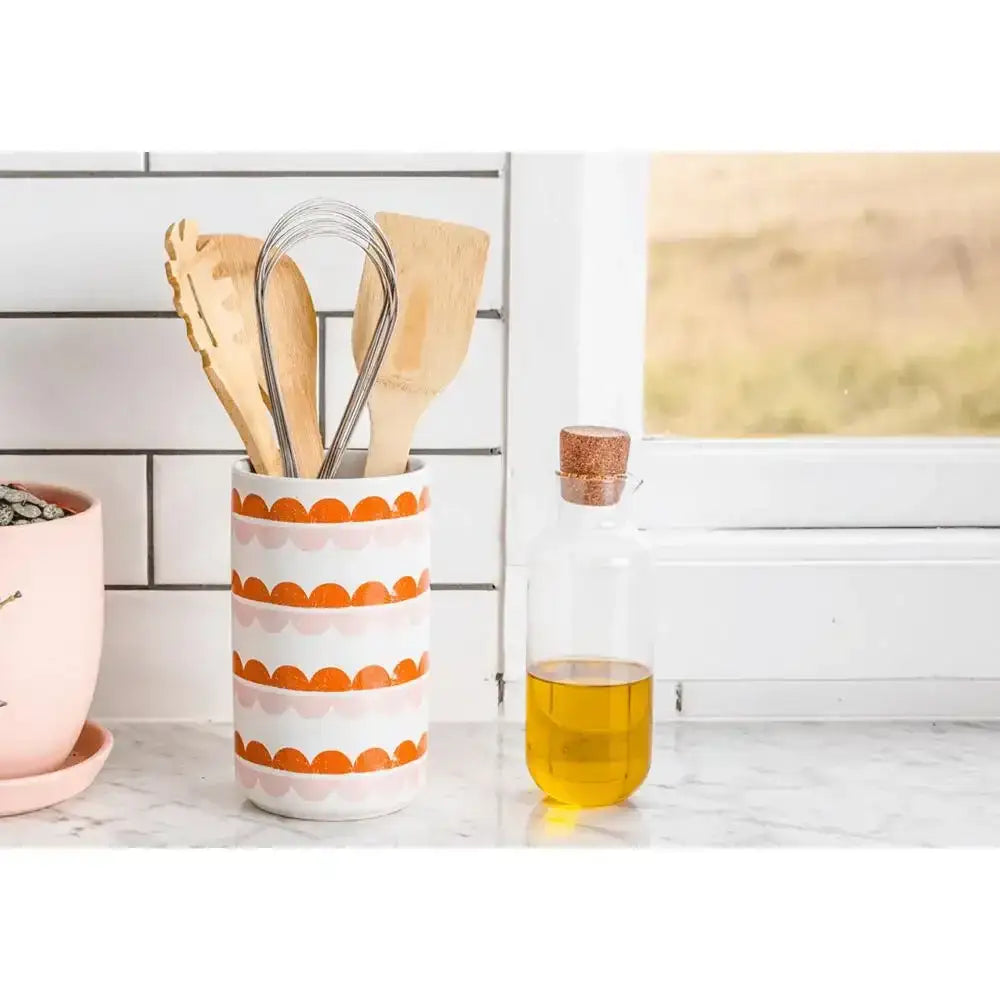 Kitchen utensils in a patterned holder next to a glass of yellow liquid on a marble countertop.