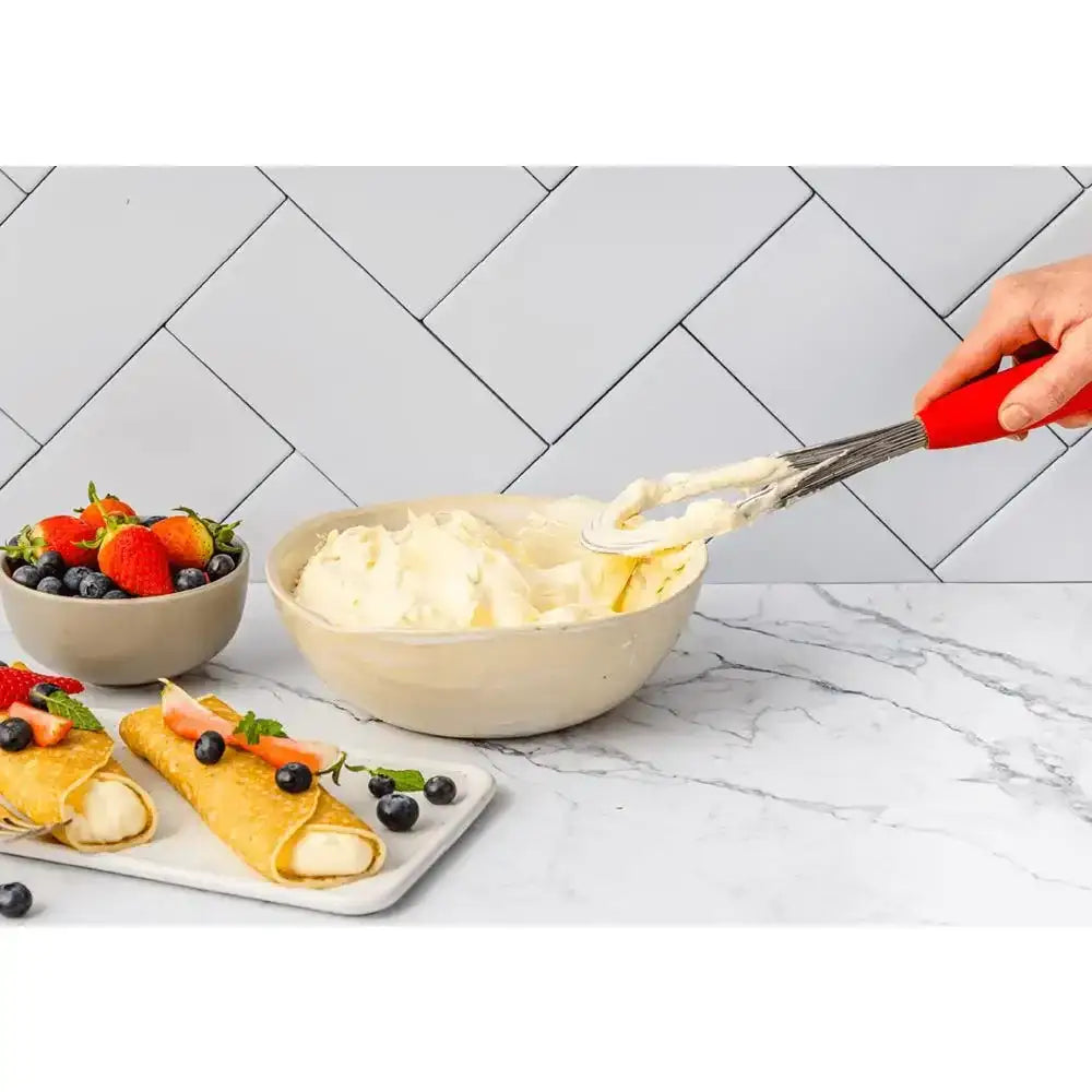 Person spreading cream on a crepe with a bowl of cream and berries in the background.