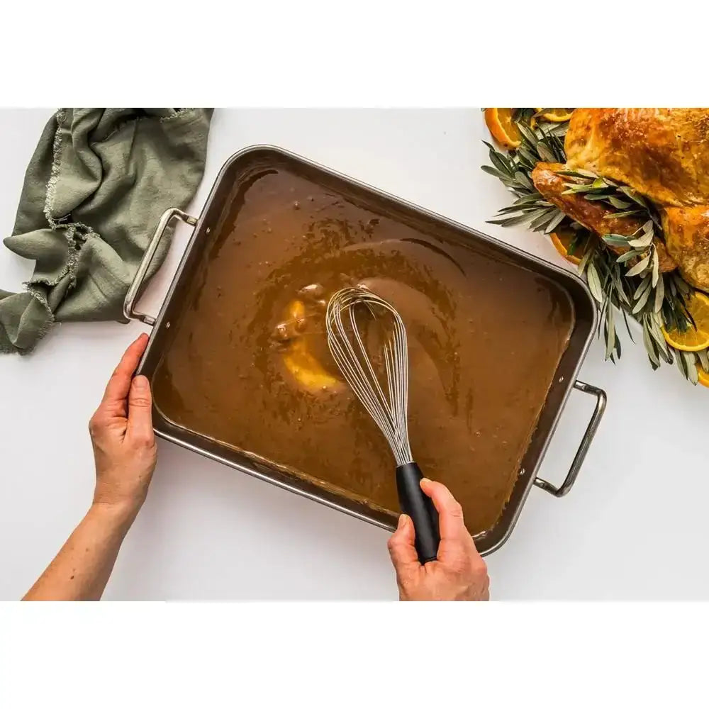 Person holding a tray of brown liquid with a whisk, next to a roasted turkey.
