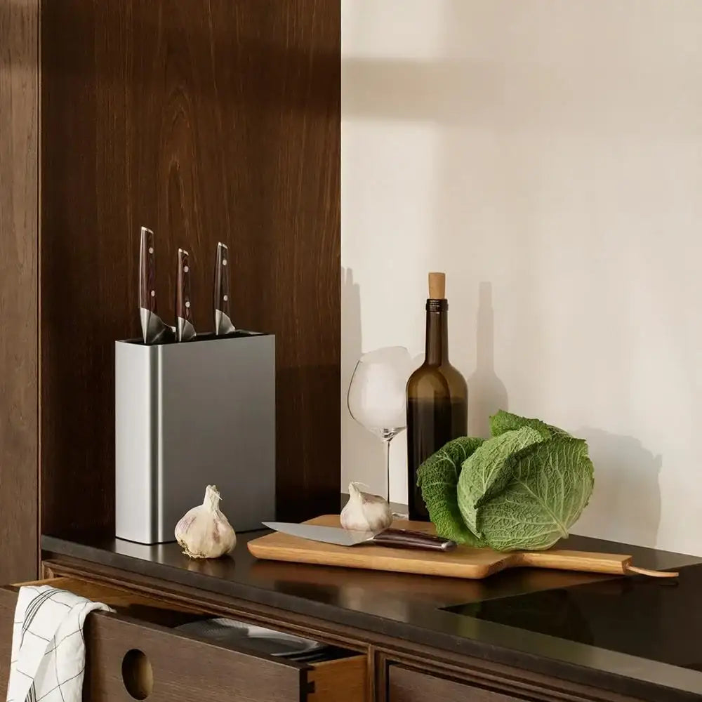 Knife block on a kitchen counter with vegetables and a bottle of wine.