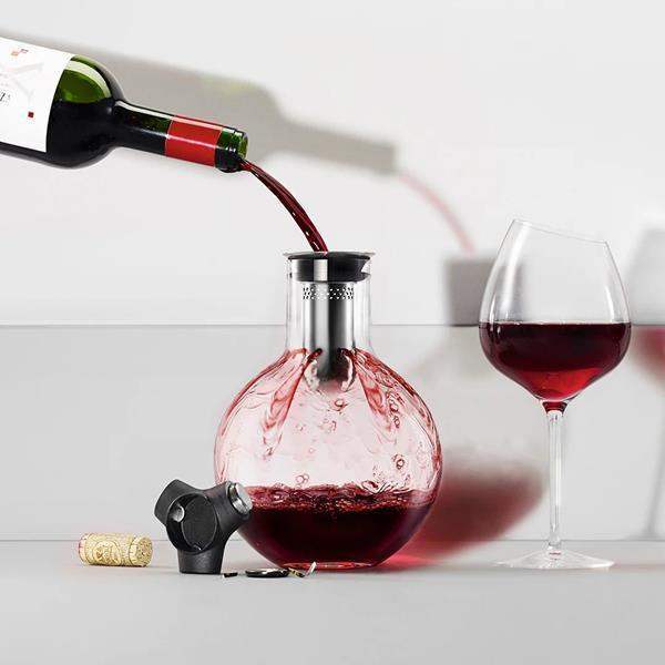 Red wine pouring into Eva Solo glass decanter carafe with wine glass, cork, and opener on table, premium kitchenware at Cookin Stores.