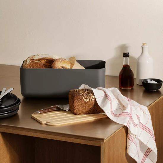 Dark gray bread bin with loaves of bread on a wooden surface with a neutral background