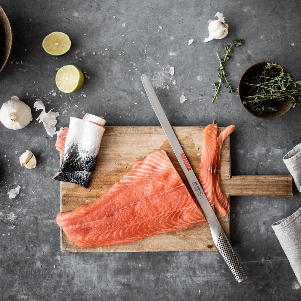 Raw salmon fillets on a wooden cutting board with a knife, lime, and garlic on a gray surface.
